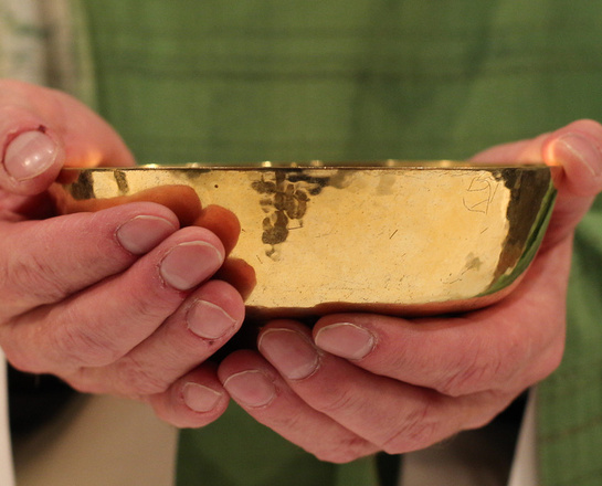 Ein Priester hält eine Patene in der Hand.